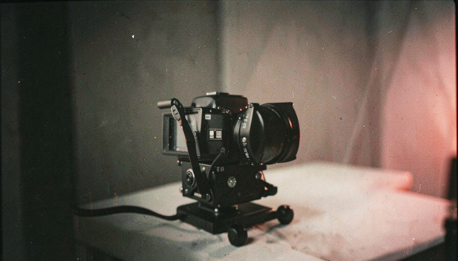 An analog photograph of a camera rig on a quiet set, deep shadows and soft highlights, moody charcoal and cream palette with grain texture