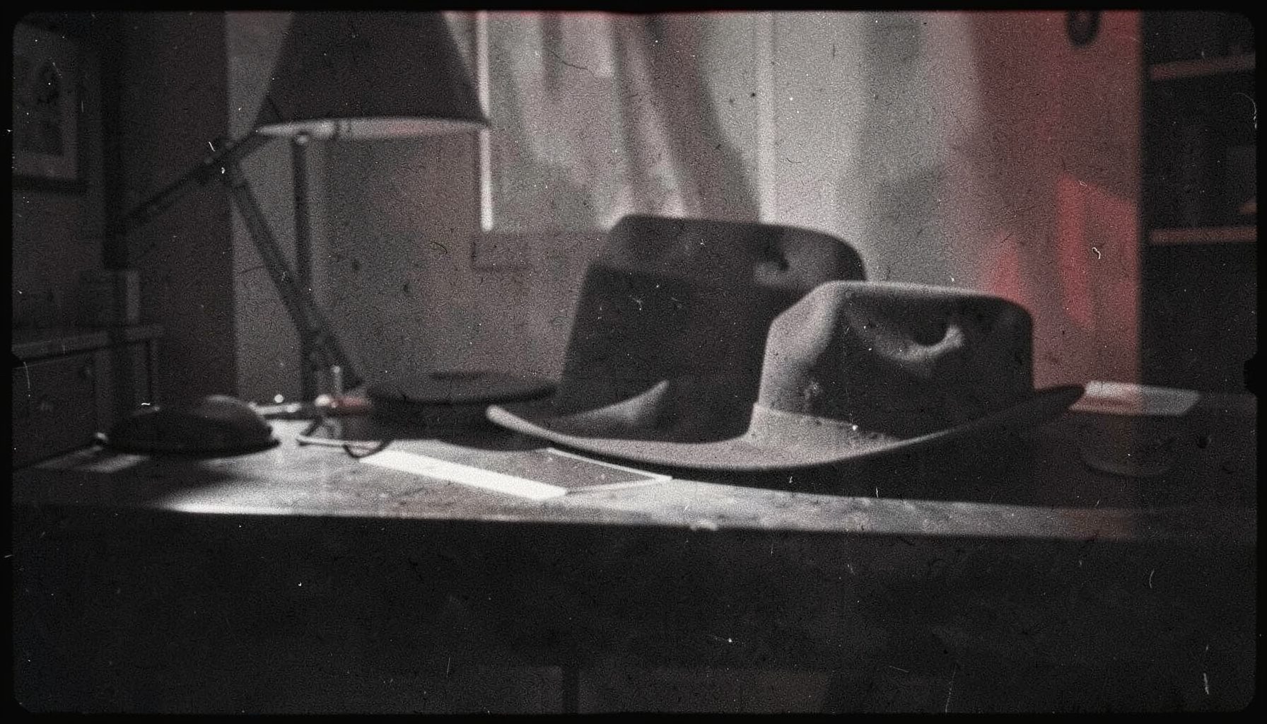 A noir-style interior with dramatic shadows and a fedora on a desk, grainy black-and-white analog photograph