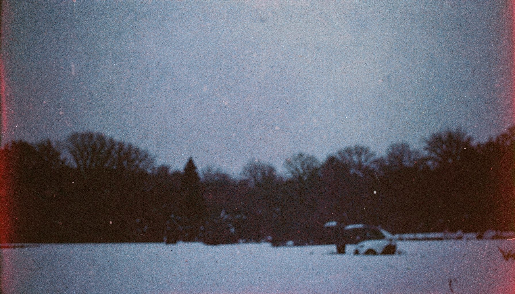A moody winter scene with a dark silhouette against snow, grainy analog film texture in muted blues and whites